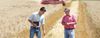 A producer marketing specialist from Providence Grain standing in a field with a farmer, looking at the crops with a red tractor in the background